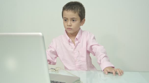 Chlapec v růžové košili si užíval sledování šťastného laptopu.Studio portrét, koncept s bílým pozadím.  - Záběry, video