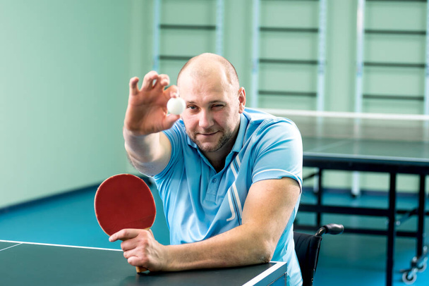 Adult disabled man in a wheelchair training before play at table tennis - Foto, afbeelding