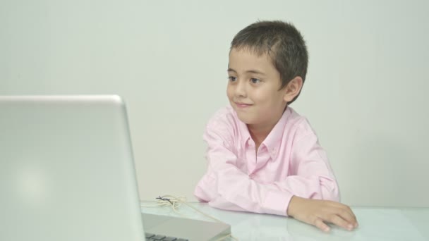 Chłopiec w różowej koszuli cieszył się oglądając laptopa szczęśliwie. Studio portret, koncepcja z białym tle.  - Materiał filmowy, wideo