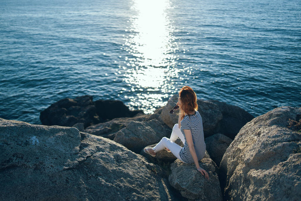 женщина путешественник сидя на камнях рядом с пляжем морской пейзаж закат чистой воды - Фото, изображение
