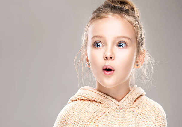 The child is a beautiful girl with wide eyes, look away in surprise. Baby in a knitted sweatshirt . Children's products , clothing and accessories . Expressive facial emotions - Photo, Image