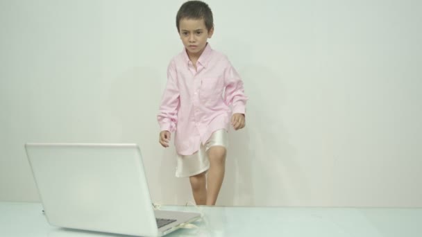 Ein Junge im rosafarbenen Hemd genoss es, den Laptop fröhlich anzusehen.Studioporträt, Konzept mit weißem Hintergrund.  - Filmmaterial, Video