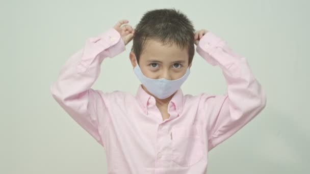 Χαριτωμένο καυκάσιο νεαρό παιδί με μπλε μάσκα προσώπου. Προστασία έναντι ιών και μολύνσεων. Studio πορτρέτο, έννοια με λευκό φόντο.  - Πλάνα, βίντεο