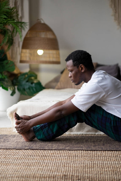 African young man sitting in paschimottanasana or Intense Dorsal Stretch pose, seated forward bend posture - Foto, afbeelding