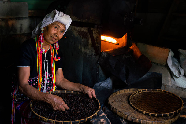 La tribu Hill tient à la main des grains de café rôtis. Vieille femme de la tribu Hill sélectionnant des grains de café devant un torréfacteur. Thaïlande. - Photo, image
