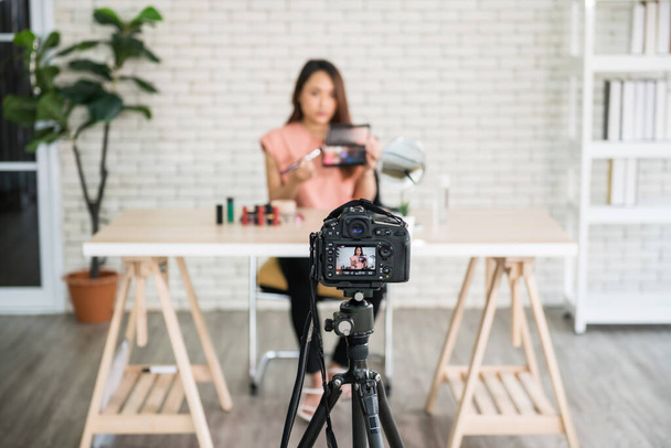 Die DSLR-Kamera zeichnet asiatische Beauty-Bloggerin auf, die Make-up für das Online-Vlog-Shopping zeigt. Kosmetik zum Verkauf per Internet-Anwendung. Berühmtes E-Commerce-Geschäft während der Covid-19-Pandemie. - Foto, Bild