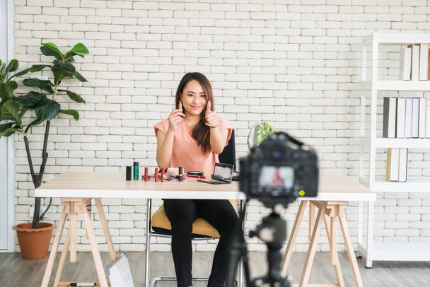 Câmera DSLR gravando blogueiro de beleza asiático mostrando batom compensar compras on-line vlog. Ela polegar para cima para vender cosméticos por aplicação de internet. Famoso negócio de e-commerce durante a pandemia de covid-19 - Foto, Imagem