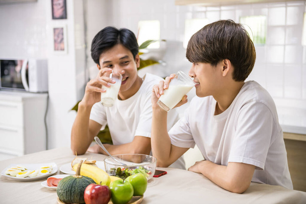 Щасливий Асаїн ЛГБТ гей-пара п'є молоко, їсть бутерброд, салат на сніданок вдома. Вони спілкуються зі усміхненим обличчям у їдальні. Одностатеві сім'ї
. - Фото, зображення