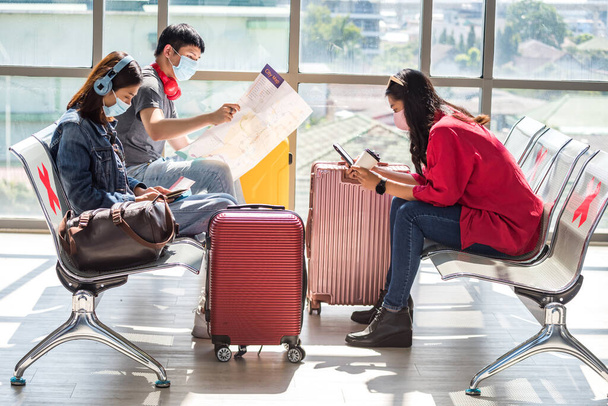 Maskeli genç Asyalı yolcular havaalanından kalkmak için bekliyor. Covid-19 salgınını önlemek için normal seyahet edin. Tatilci ya da güvenlik kavramlı tatilci. - Fotoğraf, Görsel