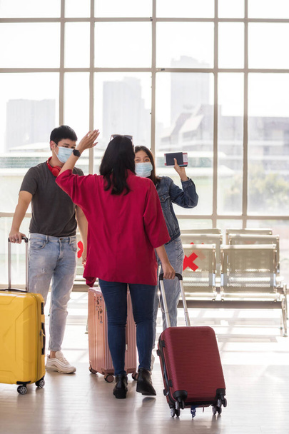 Jonge vrouw lopen en zwaaien hand aan haar vrienden met gezichtsmasker op luchthaven vertrekpunt. Meisjeshand gebaar om hallo of hallo te zeggen tegen haar metgezel. Reis met nieuw normaal om covid-19 te voorkomen. - Foto, afbeelding