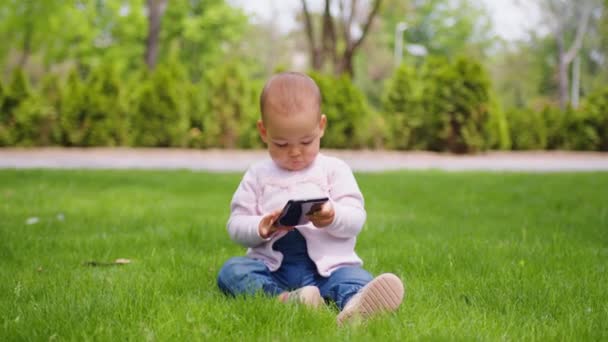 Bébé fille se concentrant sur son téléphone au parc. Bébés et technologie. - Séquence, vidéo