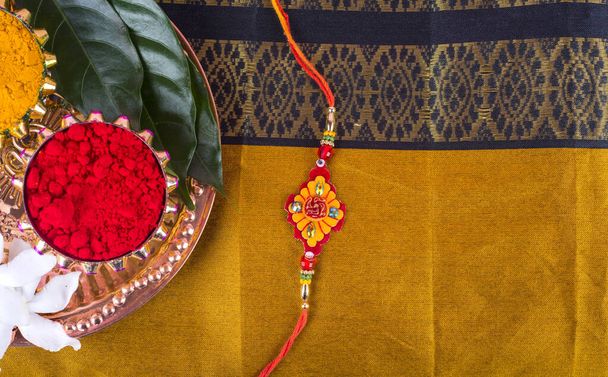 Indický festival: Rakhi s rýžovými zrny, kumkum, sladkostmi a diya na talíři s elegantním Rakhi. Tradiční indický náramek, který je symbolem lásky mezi bratry a sestrami - Fotografie, Obrázek