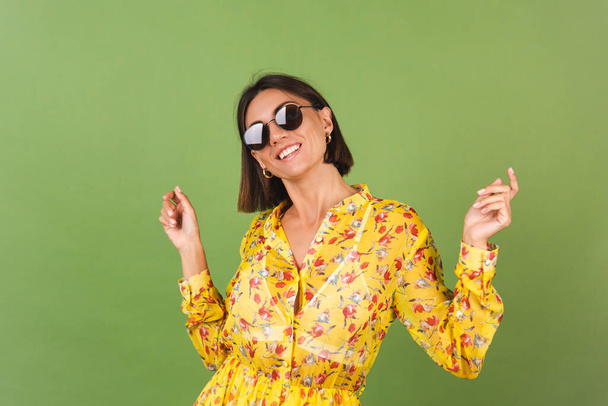 Hezká žena ve žlutých letních šatech a slunečních brýlích, zelené studio pozadí, šťastný pozitivní veselý radostné emoce - Fotografie, Obrázek