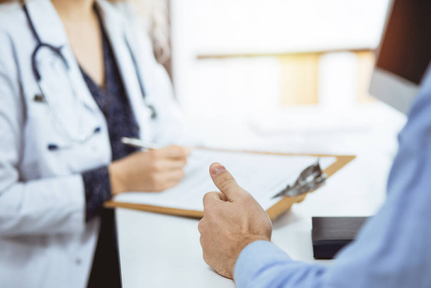 Female doctor and male patient discussing current health examination while sitting in sunny clinic, close-up. Medicine, healthcare - Photo, image