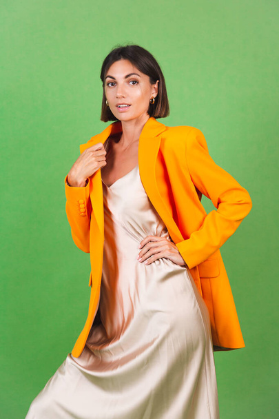 Stylish woman in silk beige dress and orange oversized blazer on green background, positive emotions smile - Φωτογραφία, εικόνα