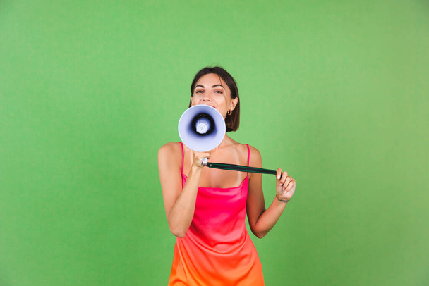 Stylish woman in pink silk dress on green background, happy excited joyful cheerful shouting in megaphone, isolated - Zdjęcie, obraz