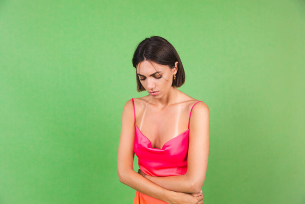 Mujer con estilo en vestido de seda rosa aislado sobre fondo verde que sufre de dolor de estómago - Foto, Imagen