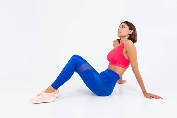 Fit tanned sporty woman with abs, fitness curves, wearing top and blue leggings on white background - Φωτογραφία, εικόνα