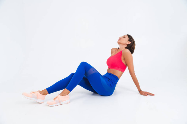 Fit tanned sporty woman with abs, fitness curves, wearing top and blue leggings on white background - Φωτογραφία, εικόνα