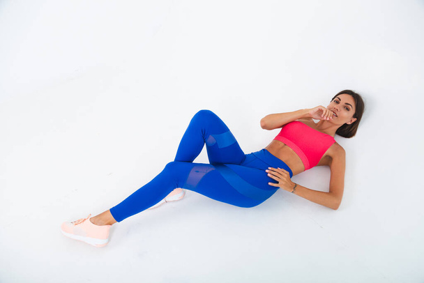 Fit tanned sporty woman with abs, fitness curves, wearing top and blue leggings on white background - Photo, image