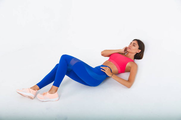 Fit tanned sporty woman with abs, fitness curves, wearing top and blue leggings on white background - Fotografie, Obrázek