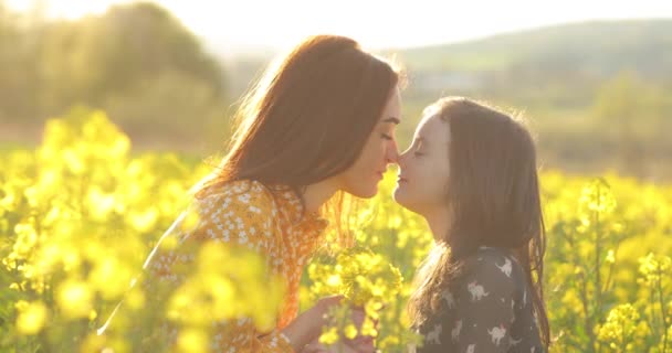 A friendly and loving family in nature. Emotional portrait of a happy and cheerful beautiful young mother playing with her little laughing daughter sitting in a field of rapeseed in the sunset light - Footage, Video