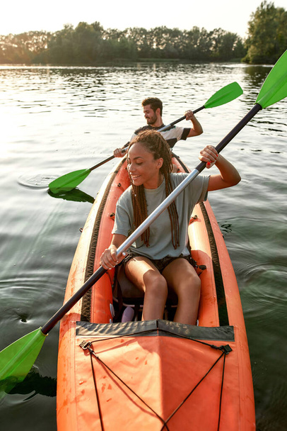 Adventurous young girlfriend paddling kayak on a river together with her boyfriend on a summer afternoon - Foto, immagini