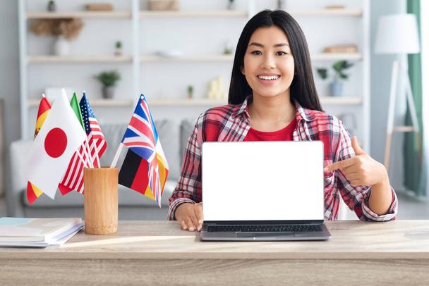 Korean Lady Sitting At Table With International Flags, Poiting At Blank Laptop - Фото, зображення