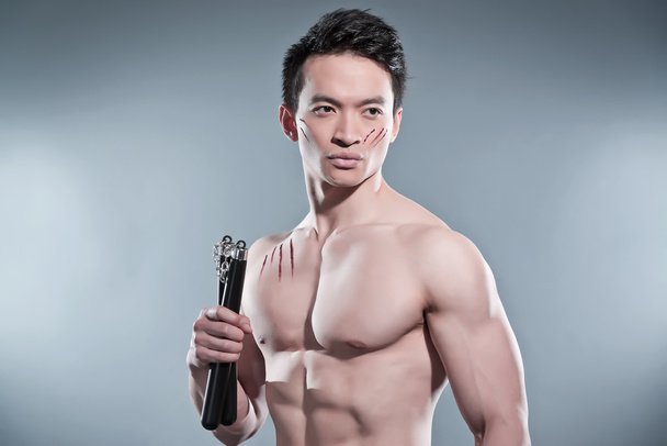 muskulöser asiatischer Kung-Fu-Mann mit Nunchucks. Blutkratzer an seinem - Foto, Bild