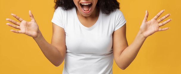 Zszokowany nierozpoznawalny czarny kobieta krzyczy i wyciąga ręce z niedowierzaniem na żółtym tle studio, panorama - Zdjęcie, obraz