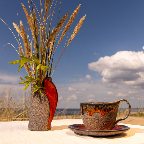 Egy agyagos kerámia váza és egy csésze csészealj elhelyezni egy vászon terítő a tengerparton - Fotó, kép