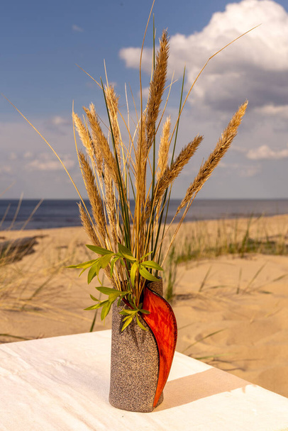 Глиняна керамічна ваза і чашка з блюдцем розміщені на лляній скатертині на морському пляжі
 - Фото, зображення