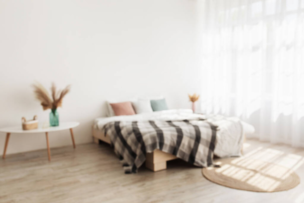 Przytulne wnętrze domu i minimalistyczny styl. Podwójne łóżko z poduszkami i kocem, stoły z suchymi roślinami w wazonach - Zdjęcie, obraz