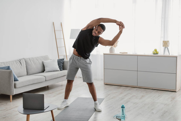 Fekete srác gyakorlása közelében Laptop csinál Side Bend Stretching Indoor - Fotó, kép