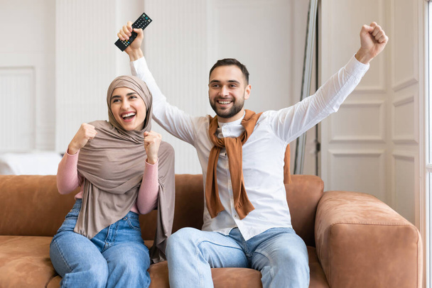 Emotionales muslimisches Paar mit Fäusten vor dem heimischen Fernseher - Foto, Bild