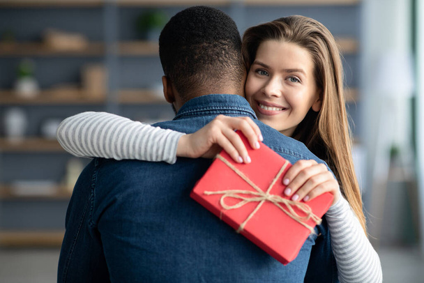Happy White Woman With Present Box In Hands Cuddling Her Black Boyfriend - Zdjęcie, obraz