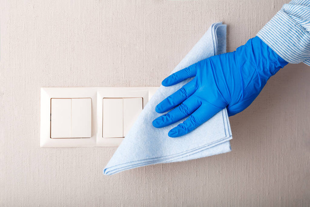 Light switch surfaces disinfection. Woman in rubber blue glove clean light switch with cloth on wall by wet rag. New normal Covid 19 coronavirus in sanitize, home cleaning. Housework clean service. - Valokuva, kuva