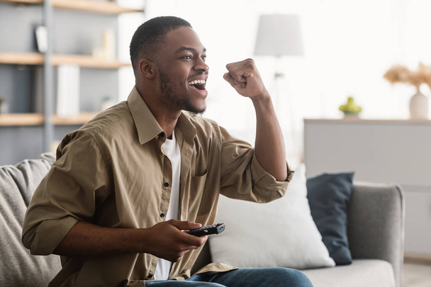 Емоційний чорний хлопець дивиться спорт на телебаченні вдома, вид збоку
 - Фото, зображення