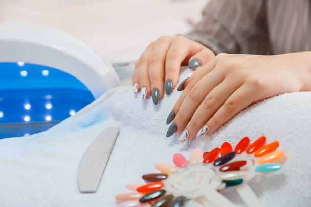 Female hands in Manicure process in beauty salon on white towel. Hygiene beauty of hands in nail salon. Woman with artificial acrylic nails picks up new polish color during manicure procedure. - Fotoğraf, Görsel