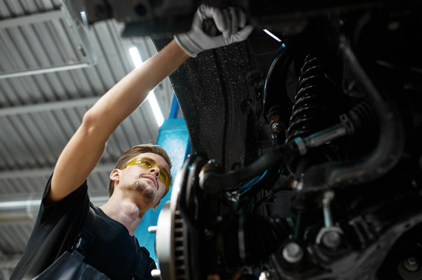 Samec mechanik kontroluje zavěšení auta, autoservis. oprava vozidel garáž, muž v uniformě, interiér stanice na pozadí - Fotografie, Obrázek