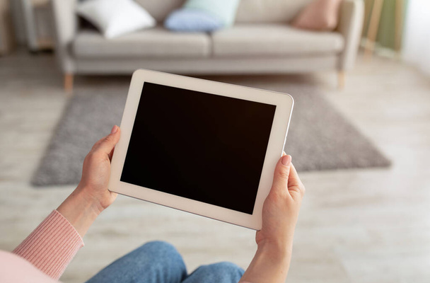 Mulher segurando tablet computador com tela vazia para publicidade app, sentado em casa no interior da sala de estar - Foto, Imagem