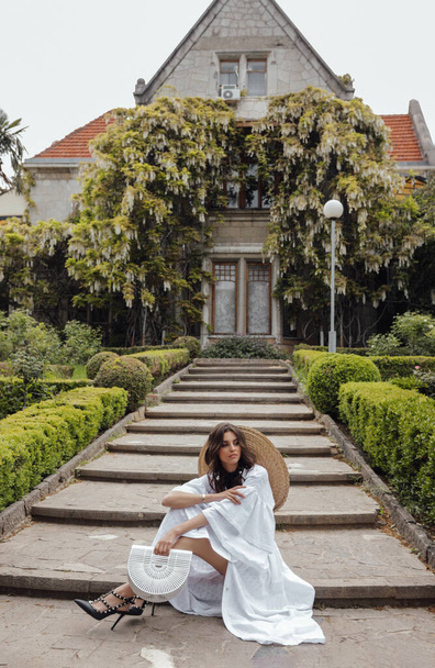 Güzel, siyah saçlı, zarif elbiseli bir kadının moda fotoğrafı. Antika bir yerdeki bahar bahçesinde poz veriyor. - Fotoğraf, Görsel