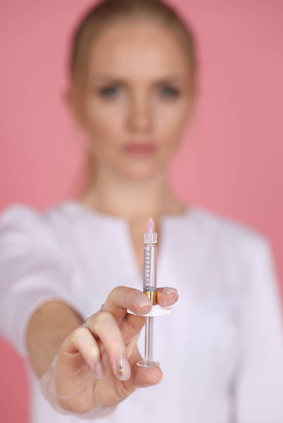 fashion studio photo of beautiful woman cometologist in white medical robe posing with injection syringe - Фото, зображення