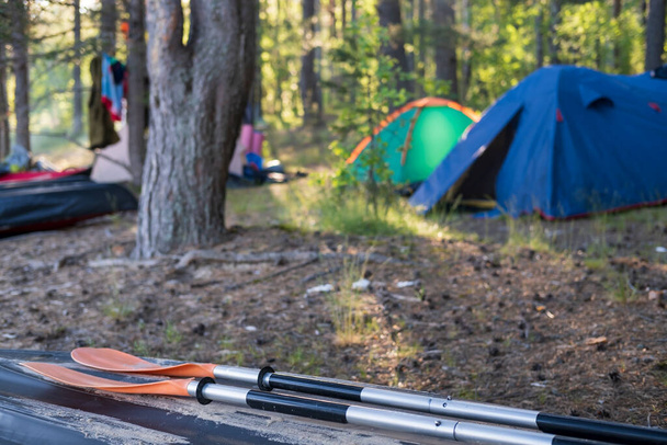 Oars lie on an overturned kayak on the shore, in the camp, against the backdrop of a tent and forest. Tourism and active lifestyle. - Photo, Image