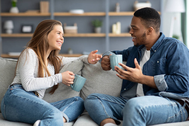 alegre interracial casal bebendo café e conversando enquanto relaxando em casa juntos - Foto, Imagem