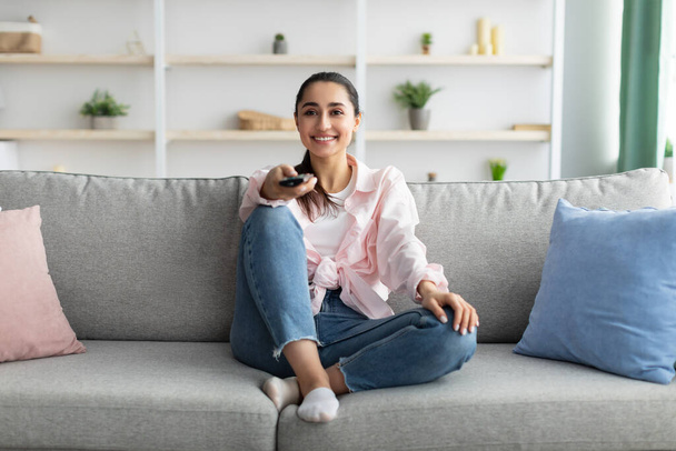Smiling woman watching tv holding remote control - Photo, Image