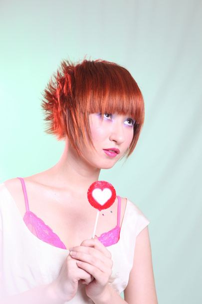 Red-haired girl with lollipop heart on blue background - Φωτογραφία, εικόνα