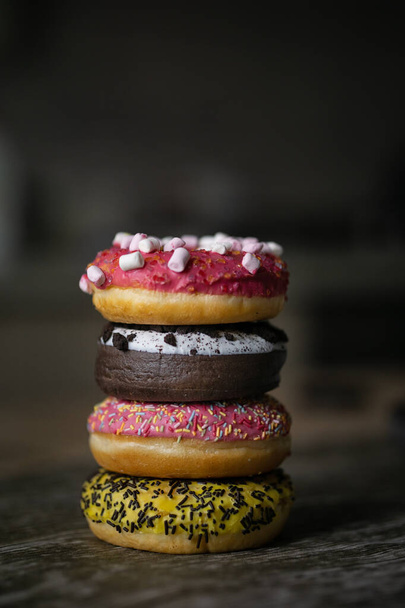 View of assortment colorful frosted delicious tasty stacked doughnuts. Colored sprinkle glazed donuts with marshmallow and chocolate - Foto, Imagem
