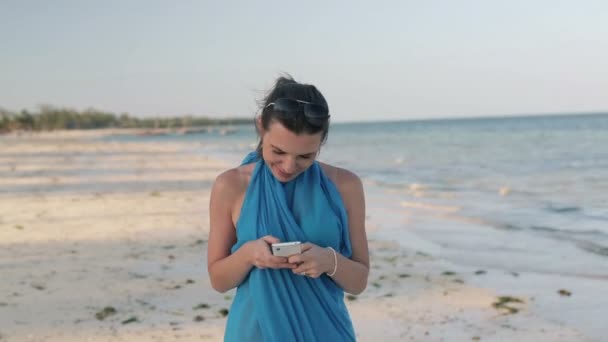 Woman with smartphone walking on beach - 映像、動画