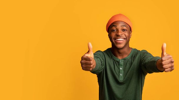 Geweldig aanbod. Vreugdevolle jonge zwarte man toont duimen omhoog bij de camera - Foto, afbeelding